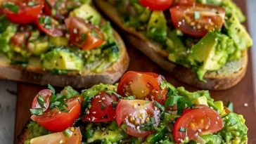 Avocadobrot mit frischen Tomaten und Basilikum auf einem Holzbrett präsentiert.